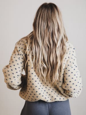 Person wearing a patterned sweater with long blonde hair, standing against a plain background