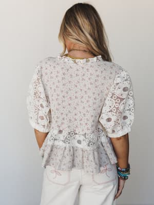 Shot from the back, this cream floral blouse with eyelet lace sleeves and a peplum hem has that effortlessly pretty energy — paired with embroidered white jeans and stacked bracelets, it feels like a farmers market morning or a bridal brunch in the b