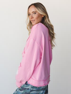 A bright candy pink oversized sweatshirt with distressed raw-hem detailing at the hem and patch accents, styled with camo joggers for an effortlessly playful, lived-in look.