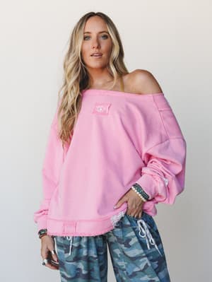 An oversized candy pink sweatshirt worn off-shoulder with blue camo wide-leg pants — effortlessly undone, the kind of outfit that looks like you threw it on and somehow nailed it.