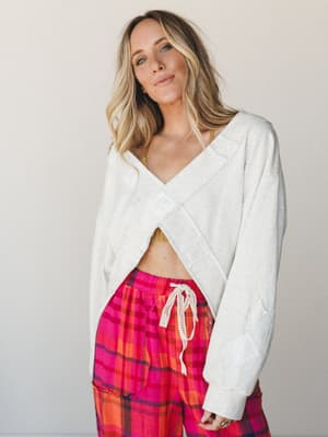 A relaxed, effortlessly cool studio shot of a cropped wrap sweatshirt in oatmeal paired with bold pink plaid pants — the kind of outfit that looks intentional at 9am without trying.