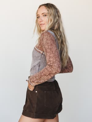 A mixed-fabric long-sleeve top with floral lace sleeves and a washed corset-style bodice, paired with dark chocolate cuffed shorts — the kind of outfit that looks effortless but definitely wasn't an accident.