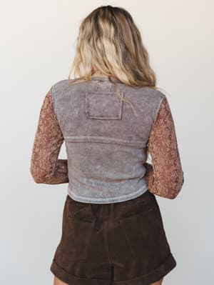 Shot from the back, this layered look pairs a washed corduroy vest over a floral jacquard long-sleeve top in warm terracotta, grounded by dark chocolate cuffed shorts — earthy, textured, and effortlessly collected.