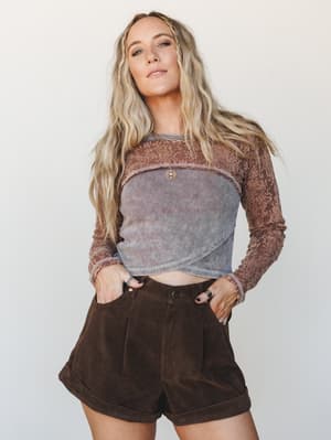 A mixed-texture crop top with lace sleeves and a ribbed corduroy-paneled front is paired with high-waisted chocolate brown cuffed shorts — earthy, layered, and effortlessly boho.