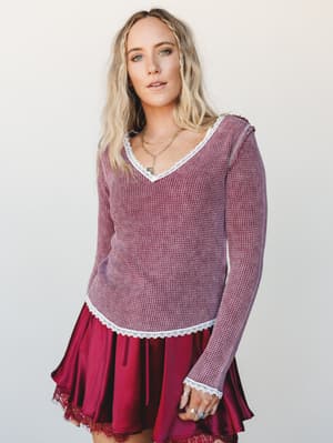 A waffle-knit long sleeve top in washed burgundy with delicate white lace trim at the neckline, hem, and cuffs, styled over a flowing crimson mini skirt — the kind of outfit that feels like fall in the best way.
