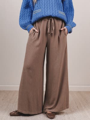 Person wearing a blue knitted sweater and brown wide-leg pants against a plain background