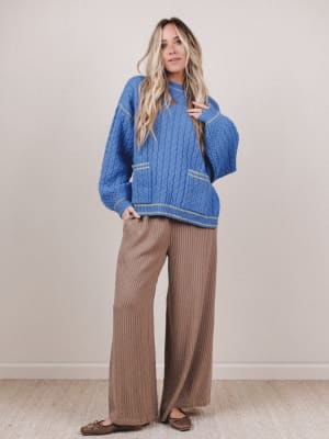 Woman wearing a blue sweater and brown pants against a plain background
