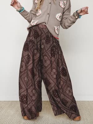 A flowing wide-leg paisley pant in deep brown paired with a taupe graphic cardigan and stacked turquoise bracelets — the kind of outfit that looks like it just came together effortlessly but definitely didn't.