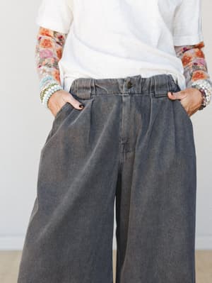 A mid-shot focused on wide-leg washed black denim trousers styled with a white tee and floral mesh sleeves — the stacked bracelets and relaxed tuck give it that effortlessly collected, lived-in feel.