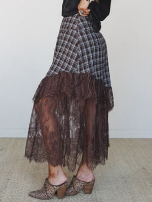 A side-profile shot of a plaid-to-lace midi skirt in deep brown — the kind of piece that looks like it was thrifted by someone with really good instincts — styled with a faded black tee and leopard print mules.