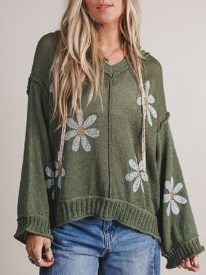 Person wearing a green sweater with floral patterns on a plain background