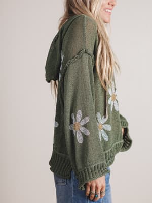 Green hoodie with floral patterns worn by a person on a plain background