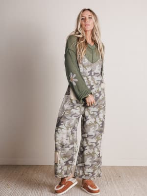 Woman wearing a green sweater and camouflage pants with a neutral background