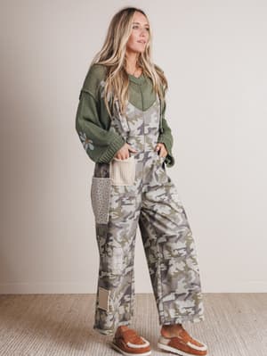 Woman wearing a green sweater and camouflage overalls against a plain background