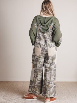 Person wearing a green hoodie and camouflage overalls with a plain background