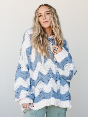 An oversized wavy-knit hoodie in cornflower blue and cream worn with sage green pants — the kind of sweater that looks like it was made by a very stylish grandmother and you mean that in the best possible way.