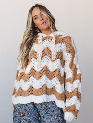 An oversized crochet-knit hoodie in ivory and camel chevron waves styled with butterfly-print wide-leg pants — cozy and expressive in equal measure, the kind of outfit that looks effortless but is clearly intentional.