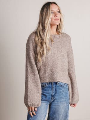 Woman wearing a brown sweater and blue jeans against a plain background