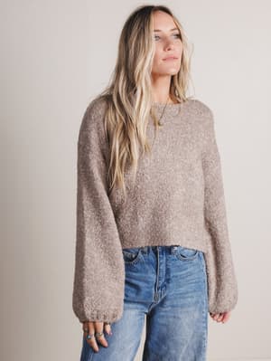 Woman wearing a brown sweater and blue jeans against a plain background