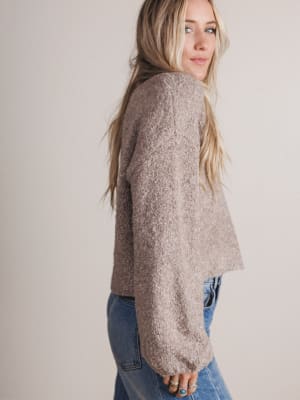 Woman wearing a beige sweater and blue jeans against a plain background