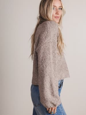 Woman wearing a beige sweater and blue jeans against a plain background