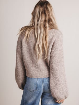 Person wearing a beige sweater and blue jeans against a plain background