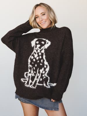 An oversized chocolate brown knit sweater with a bold intarsia Dalmatian graphic worn casually over a denim mini skirt — the kind of piece that makes everyone in the coffee shop ask where you got it.