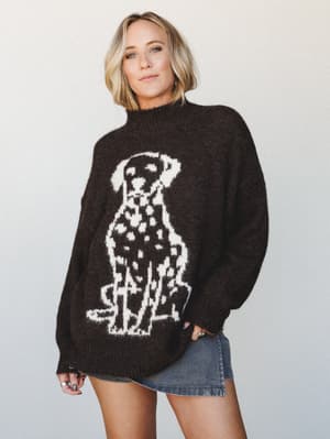 An oversized chocolate brown knit sweater with a large intarsia Dalmatian graphic takes center stage here — worn with a denim mini skirt and stacked rings, it has that perfectly personality-forward, cozy-cool energy.