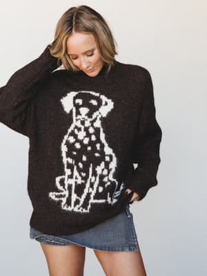 An oversized chocolate brown knit sweater with a large intarsia Dalmatian graphic takes center stage here — worn with a denim mini skirt and that easy, slightly-distracted energy of someone who genuinely loves her sweater.