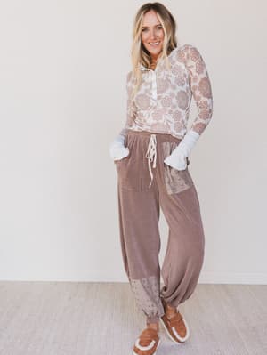 Woman wearing a lace top and brown pants with a white background