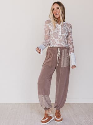 Woman wearing a lace top and brown pants with a white background