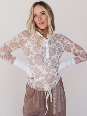 Woman wearing a floral lace top and brown pants against a plain background
