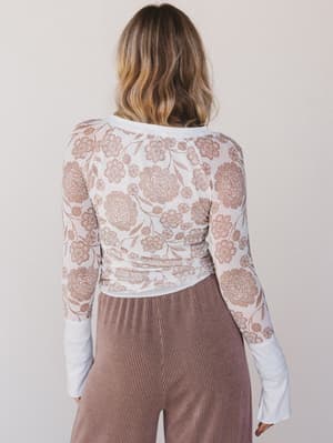 Person wearing a floral lace top and ribbed pants against a plain background