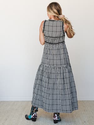 A back-facing shot of a tiered gingham maxi dress styled with printed western boots — the black-and-white check paired with those teal and cow-print booties gives it that effortless boho-country energy that just works.