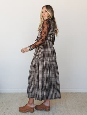 A tiered gingham midi dress with sheer lace sleeves and a chocolate-and-cream plaid pattern, styled with wood-sole clogs and layered boho jewelry — the kind of outfit that feels equally at home at a farmers market or a fall brunch.