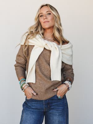 A relaxed, put-together look featuring a warm mocha knit sweater layered with a cream scarf tied at the chest, paired with dark denim — the kind of outfit that looks effortless but clearly wasn't an accident.