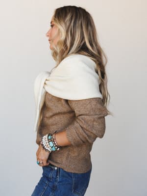 A side-profile shot of a model in a cozy mocha knit sweater layered with a cream wrap scarf, stacked turquoise and beaded bracelets adding that collected, expressive finishing touch against a soft neutral studio backdrop.
