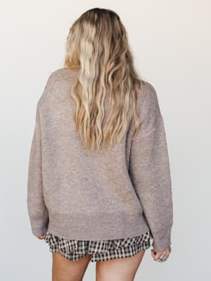 Shot from the back, a relaxed oversized sweater in warm sand-taupe pairs effortlessly with a gingham ruffle mini skirt — the kind of thrown-together combo that somehow looks completely intentional.