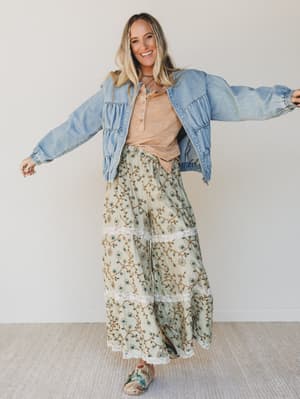 Woman wearing a denim jacket and floral pants with a plain background