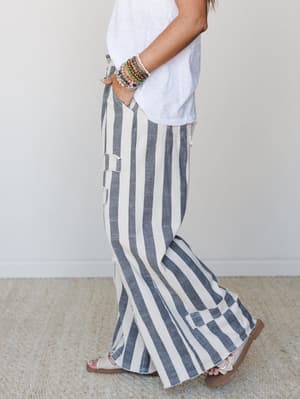 A side-profile shot of wide-leg striped pants in charcoal and cream, styled with a relaxed white tee, flat sandals, and a stack of colorful beaded bracelets — the kind of outfit that looks effortless but definitely wasn't an accident.