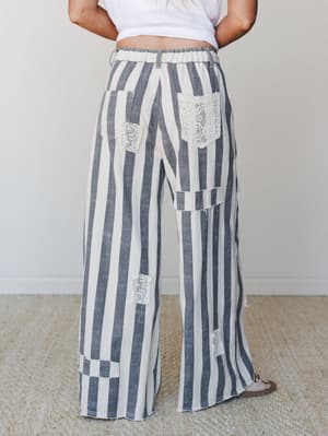 Back view of wide-leg striped pants with crochet patch detailing — the kind of pants that feel like a statement without trying too hard, worn with a cropped white tee and sandals.