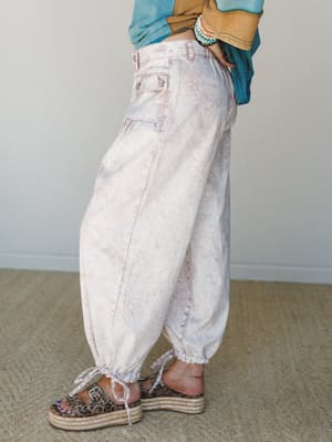 A side-angle shot of relaxed, balloon-fit cargo jeans in a soft pink marble wash, styled with a layered teal and mustard top, stacked bracelets, and leopard print platform sandals — the kind of outfit that looks effortless but definitely wasn't an ac