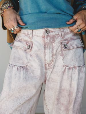 A close-up of acid-washed cargo-style wide-leg jeans in a dusty pink marble wash, styled with a teal sweatshirt and layered silver and turquoise jewelry — the kind of outfit that looks effortless but absolutely took thought.