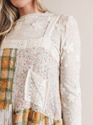 Close-up of a person wearing a white lace top with a colorful plaid pattern underneath.