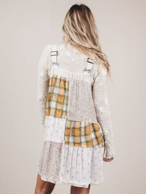 Person wearing a dress with plaid pattern and suspenders on a plain background