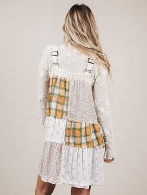 Person wearing a dress with plaid pattern and suspenders on a plain background