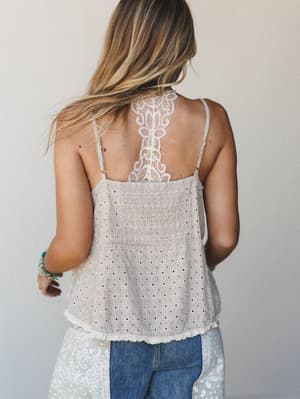 A back-facing shot of a model in a breezy eyelet cami with a standout lace racerback detail — the kind of top that looks just as good from behind as it does from the front, tucked into jeans or layered under a cardigan.