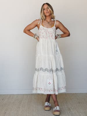 A cream tiered maxi dress with delicate floral embroidery and eyelet texture, styled with platform espadrille sandals and layered boho jewelry — the kind of dress that works as hard at a bridal shower as it does wandering a farmers market.