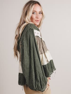 Woman wearing a green patterned cardigan over a beige top on a plain background