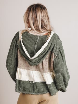 Person wearing a green hooded sweater over a sheer top and skirt on a plain background